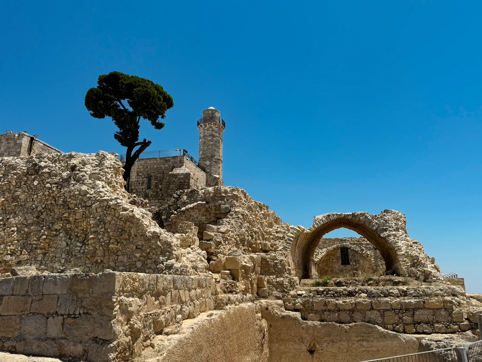 A hilltop fortress ruin with a lone tree and a stone watchtower against a deep blue Israeli sky.